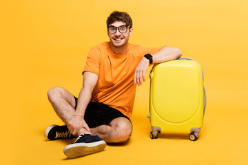 cheerful male tourist sitting near travel bag for summer vacation on yellow