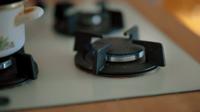 A flame bursting out of one of the eyes of a gas stove next to a pot