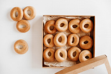 Drying or round bagels in a paper box on a white wooden background. Top view. Copy, empty space for...