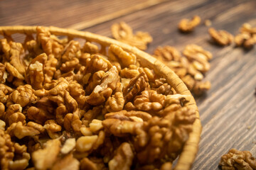 Peeled walnuts in a wicker basket and peeled walnuts scattered on a wooden table. Healthy diet. Fitness diet. Close up.