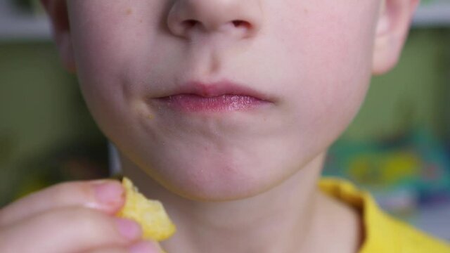 Young caucasian kid eating unhealthy potatoes crisps. Smiling boy enjoys chips.  Child puts potato chips in his mouth. Snack on junk food. Portrait of a boy with a satisfied face. Tasty food.