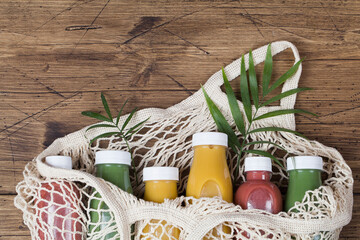 yellow green and crimson smoothie in mesh bag on brown wood background, served in bottle with palm leaf