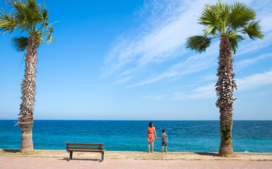 A woman with a child stands on the promenade and looks at the sea