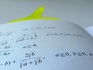 printed math exercise on clear white paper. a book page. black text with math symbols and numbers. exam materials. low angle view. blurred background. study and education concept. selective focus