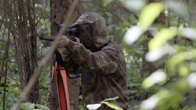 Hunter in camouflage clothes takes aim while standing from hunting rifle. Man in comfortable camouflage clothes hunter outdoor in forest hunting alone. Outdoor activity concept.
