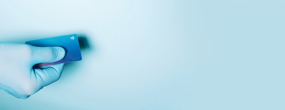 Contactless payment concept, copy space. Hand in protective gloves holding credit card with contactless symbol, electronic chip. Online shopping, online banking. Payment by plastic cards.