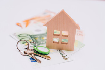 wooden house with keys stands on banknotes on a white background
