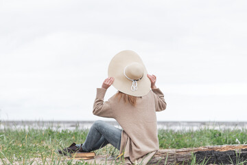 A woman dressed in a warm cardigan and a beige hat looks at the sea at sea during a storm