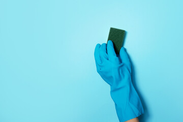 Hand in glove holding microfiber cleaning cloth, sponge on blue background. Copy space. Cleaning...