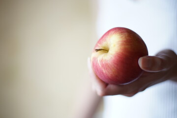 Red apple in female hand on the background of a girl in a white shirt. Copy space.