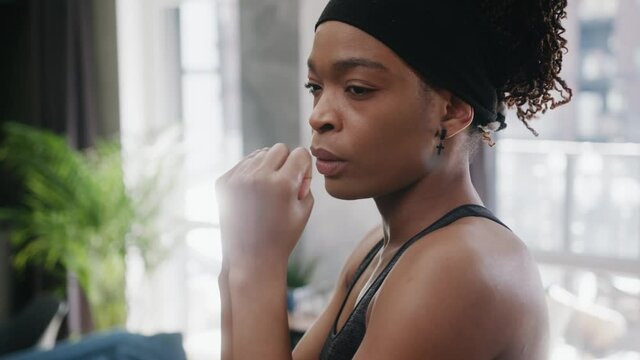 Confident strong black young fit woman athlete boxing fists punching the air doing training warm-up sports routine indoors. Home isolation. Fitness. Workout.