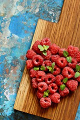Heart shape made of premium raspberries on a wooden board on a blue background. Close up, top view. Romantic concept. Valentine's day symbol
