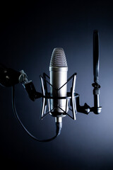 Condenser podcasting microphone in dramatic light with pop filter on black background
