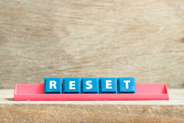 Tile letter on red rack in word reset on wood background