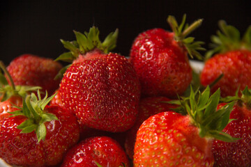 Strawberry in a white plate close up on a black background. Fresh red strawberry in white bowl on black background. side view, copy space, close up.