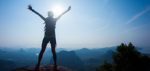 Cheering woman hiker outstretched her arms at sunrise mountain peak