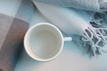 Empty enamel mug and blue check plaid on the table.