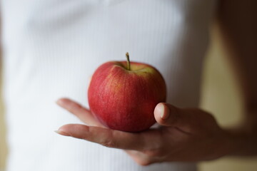 Red apple in young female hand on the background of a girl in a white shirt