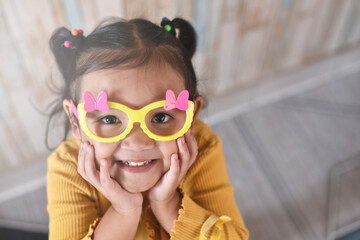 High Angle view of a smiling little asian girl wearing fancy glasses. Concept of happy child and emotions