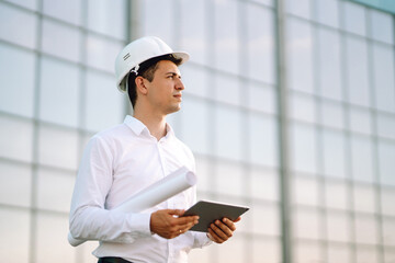 Young worker in a helmet and with a tablet at a work object. Male engineer at a construction site...