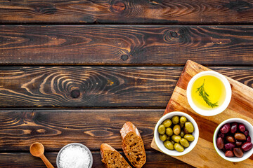 Olives and olive oil in bowls on cutting board on wooden top view copy space