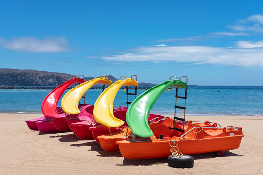 Colorful water slide boats, docked on the empty sandy beach, retired for the lockdown and no tourism, on one of the popular beaches on the island Playa de Camison, in Tenerife, Canary Islands, Spain