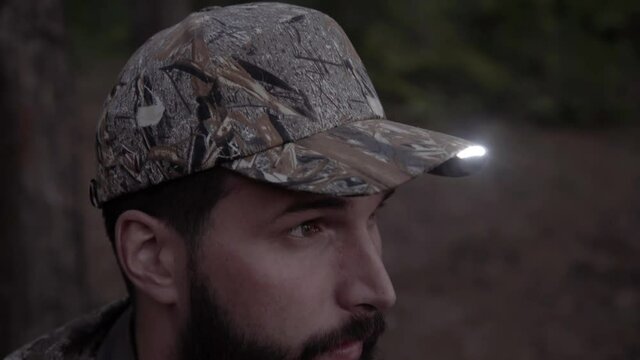 Portrait of handsome young man hunter or tourist. Man puts on his head cap with diode flashlight on visor in evening.