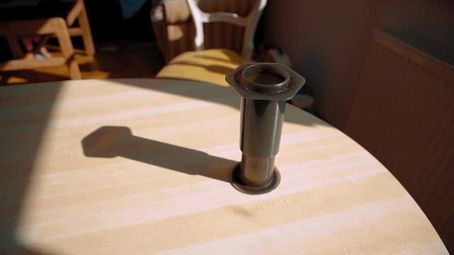An aeropress brewing fresh coffee on a wooden table in the sunlight with its shadow next to it.