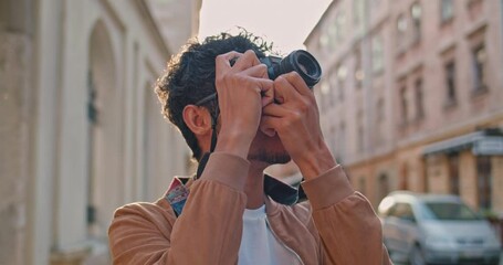 Crop view of young man with nose ring taking photo of city scape. Handsome male tourist in glasses standing at old city street. Concept of travelling, tourism and photography - Powered by Adobe