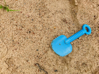 Fototapeta na wymiar Child's shoulder blade on wet sand. Blue blade in sand on beach. Abandoned, forgotten toy shovel. Concept summer children's recreation after quarantine. Texture sand. Place for an inscription or logo