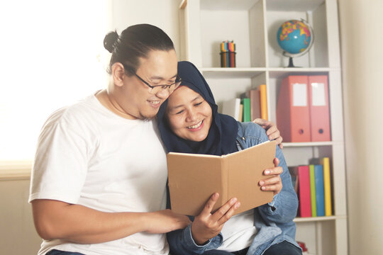 Young Asian muslim couple reading book together, happy cheerful expression, new married planning their future