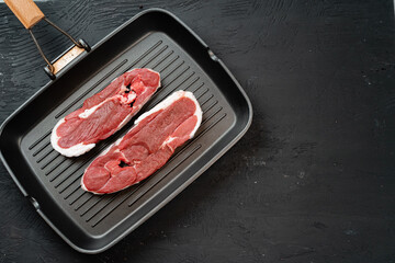 Raw steak on frying grill pan. Dark background.
