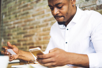 Obraz premium Concentrated afro american administrative manager dressed in elegant white shirt dialing number from visit card planning to have conversation with marketing expert providing advertising consultation