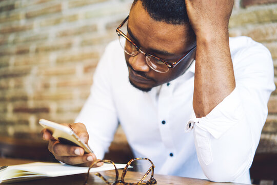 Concentrated handsome afro american food blogger chatting with followers answering question about publishing advertising content and collaboration via smartphone connected to free 5G wireless