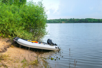 white motorized PVC inflatable boat moored on the sandy shore of the lake against a cloudy sky