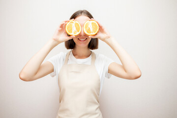 Beautiful girl in apron with oranges. Young woman covering her eyes with halves of orange