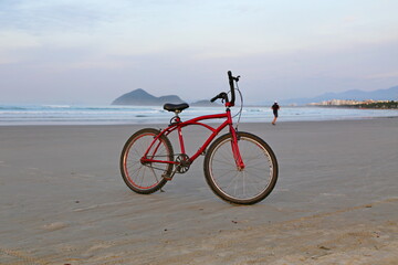 Obraz premium A red bike on the beach sand. In the background a man running. The sea, blue ocean and the horizon. Brazil, Bertioga, Sao Lourenco beach.