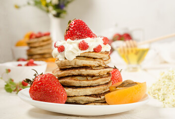 A stack of pancakes with whipped cream, strawberries and fruit close-up. Tasty summer breakfast.