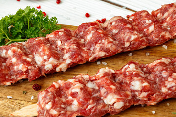 Raw lula kebab on skewers with spices on wooden board