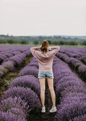Young woman standing in lavender field, between rows of lavender bushes.