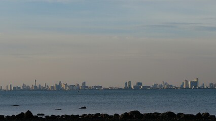 The beach view has rocks spread out into the sea. The background is a city