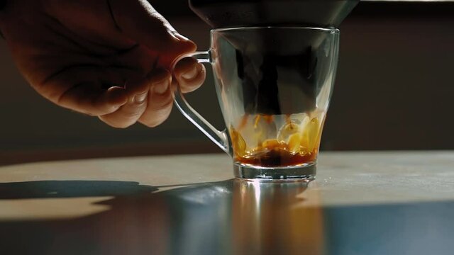 Coffee being pressed through an aeropress into a transparant cup held by a man's hand