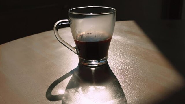 A cup of coffee with the shadow of the cup on a wooden table