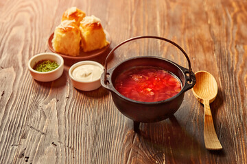 Traditional Ukrainian Russian vegetable borscht on an old wooden background in portioned cast iron. With herbs, sour cream and garlic bread
