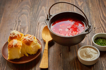 Traditional Ukrainian Russian vegetable borscht on an old wooden background in portioned cast iron. With herbs, sour cream and garlic bread