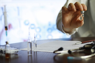 A man signs a medical document. Medical equipment on the table. Stethoscope and ampoules with syringes. Makes notes in the office. Medical center.