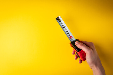Hand holding tape measure on yellow background.
