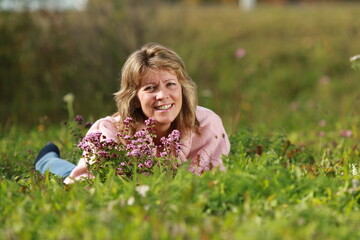 Senior woman lying in the grass with flowers around her