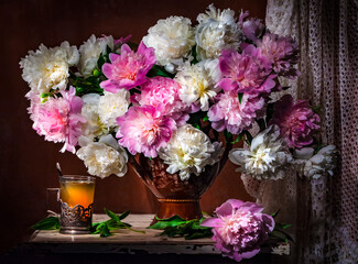 Fototapeta premium Classic still life with bouquet of beautiful white and pink peonies and a glass of tea in a Russian glass holder a ray of light on brown background . Art photography.