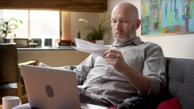 Man looking through his stack of mail, opens up an envelope with a bill and gets stressed out